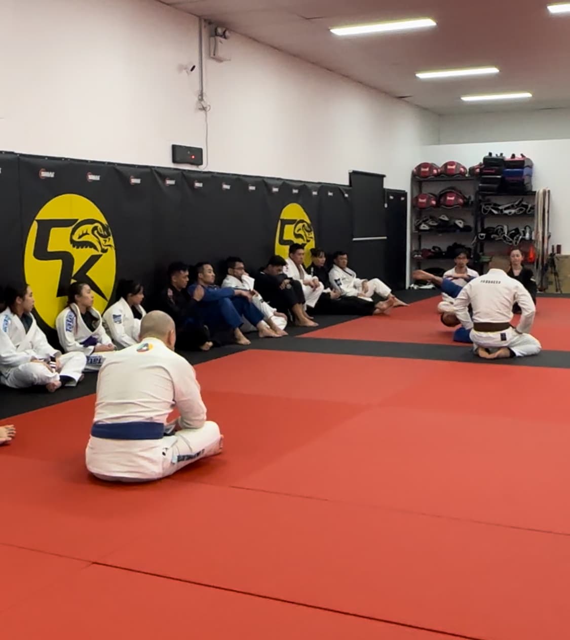 Gi jiu-jitsu class seated on the mats listening to the instructor